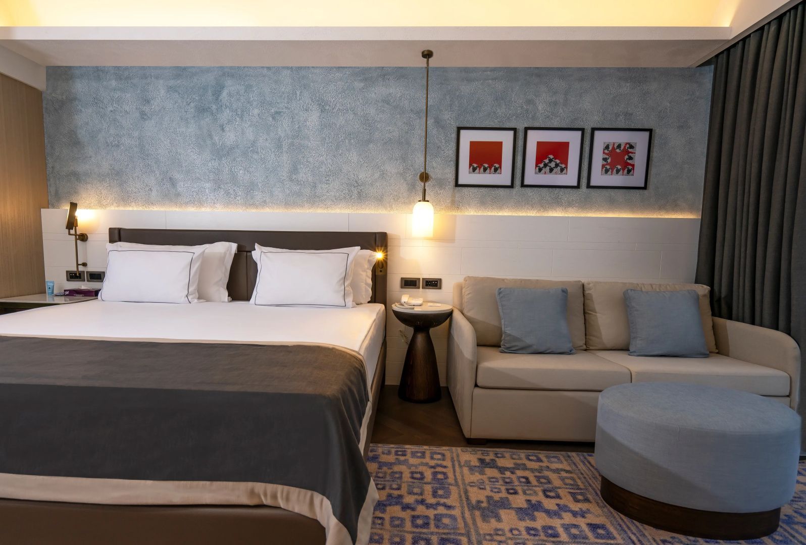 Doppelbett mit weißer Bettwäsche, ein beiges Sofa und eine blaue Wand im Hotelzimmer.