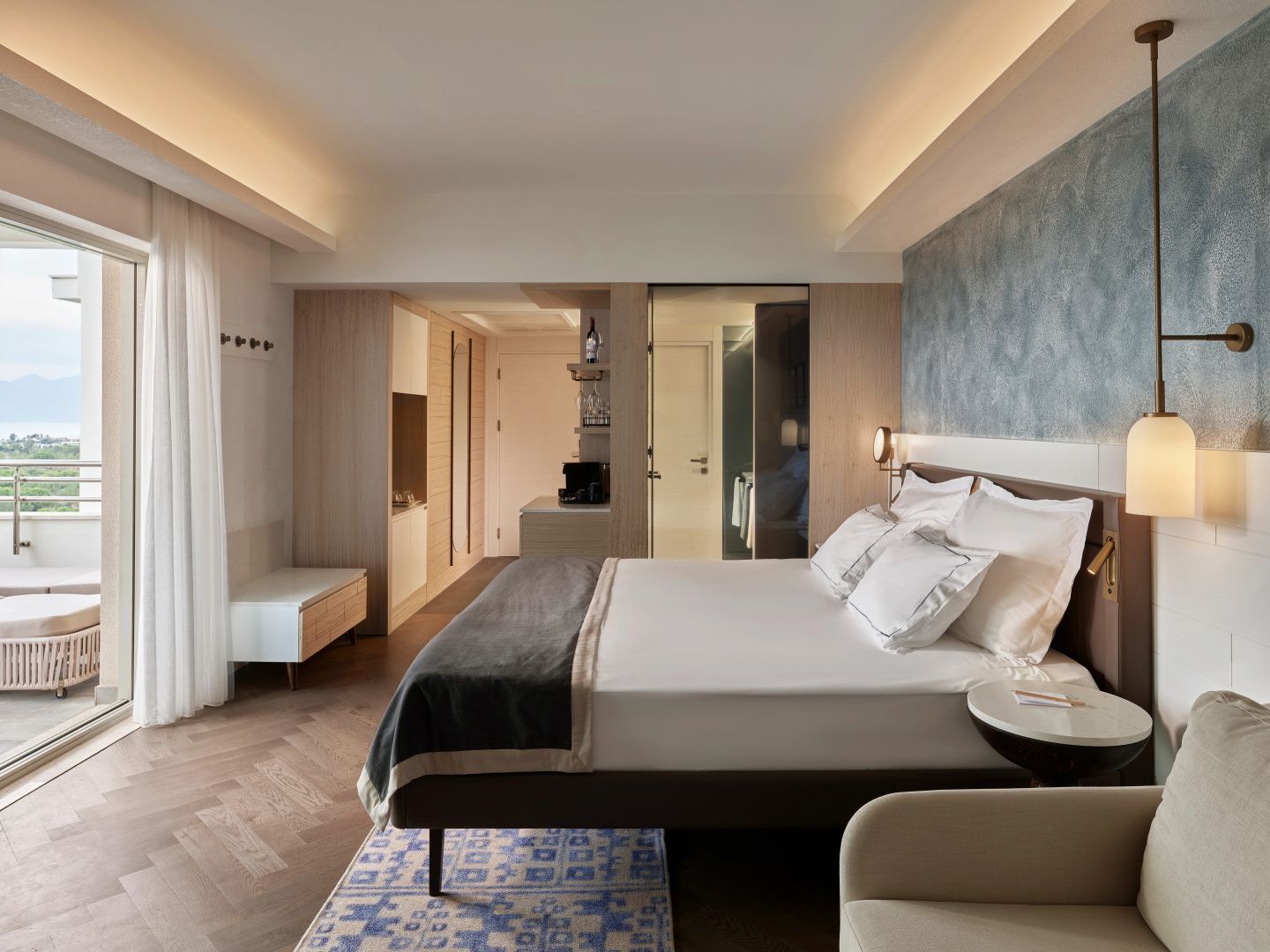 Doppelbett mit weißer Bettwäsche in einem hell eingerichteten Hotelzimmer mit Holzfußboden.
