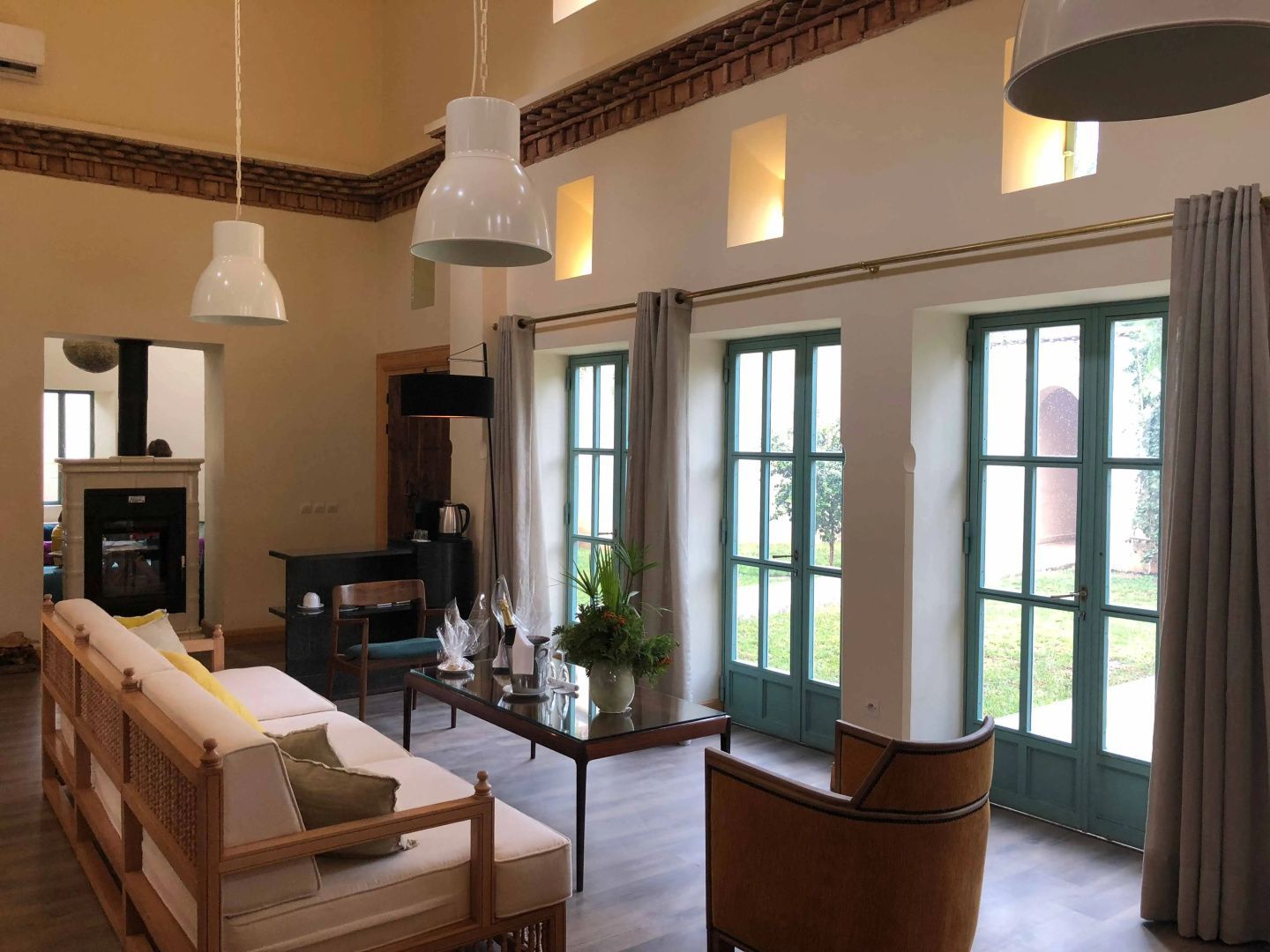 Lichtdurchfluteter Wohnraum mit hohen Decken, hellem Sofa und drei hohen Glastüren mit grünem Rahmen.