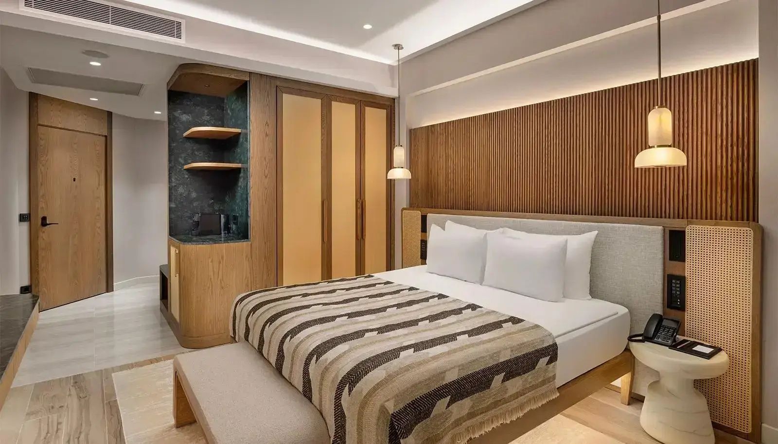 Doppelbett mit gestreifter Tagesdecke, Holzschrank und Holzverkleidung im Hotelzimmer.
