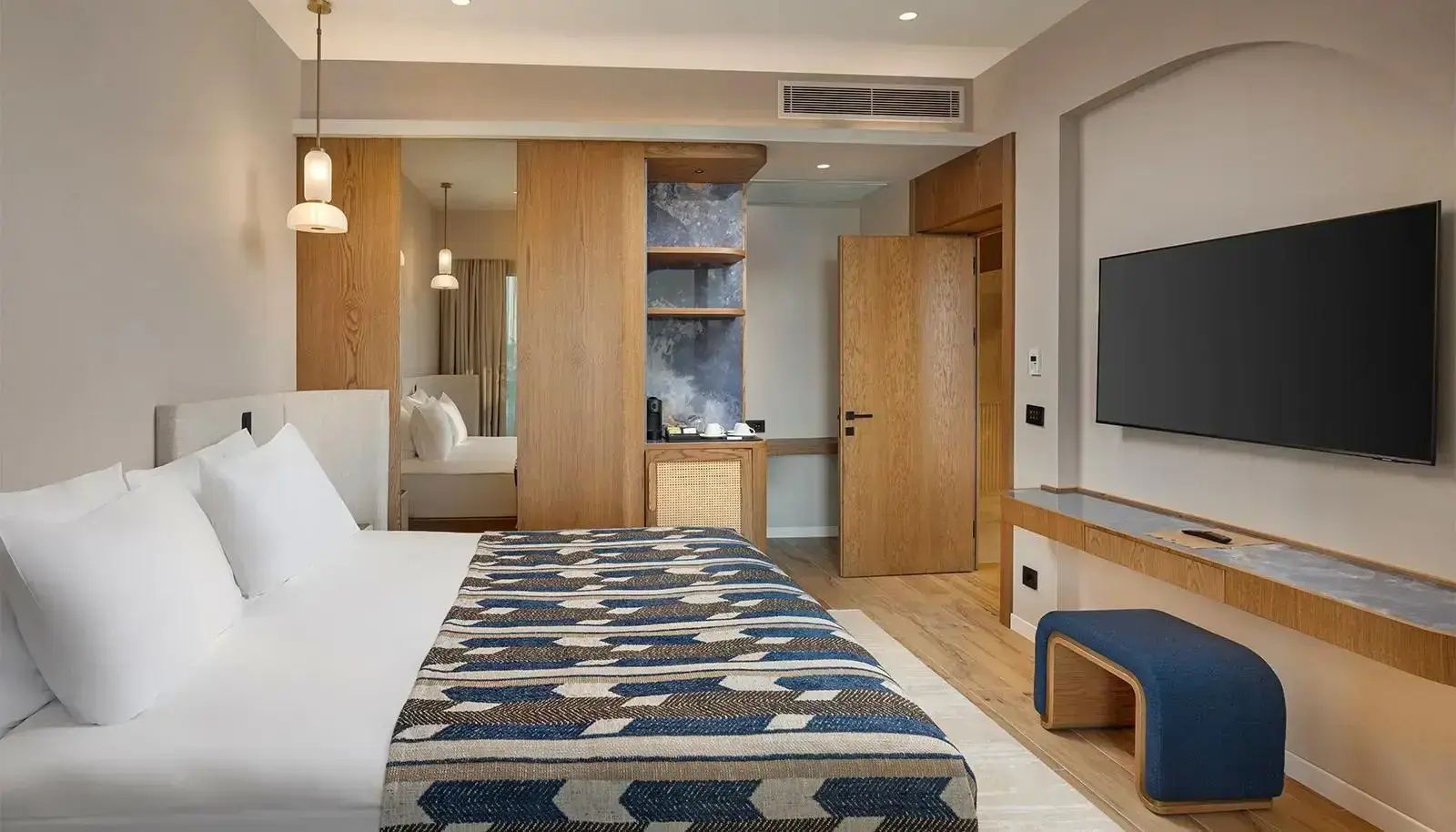 Doppelbett mit blau gemusterter Tagesdecke in einem hellen Hotelzimmer mit Holzverkleidung.