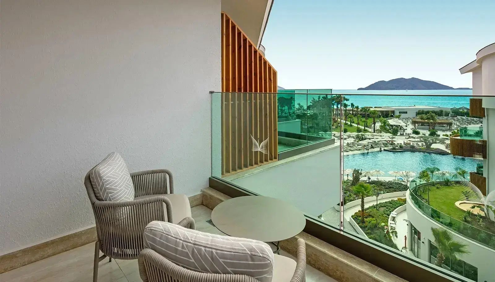Balkon mit zwei Sesseln und Blick auf die Poolanlage sowie das Meer im Hintergrund.