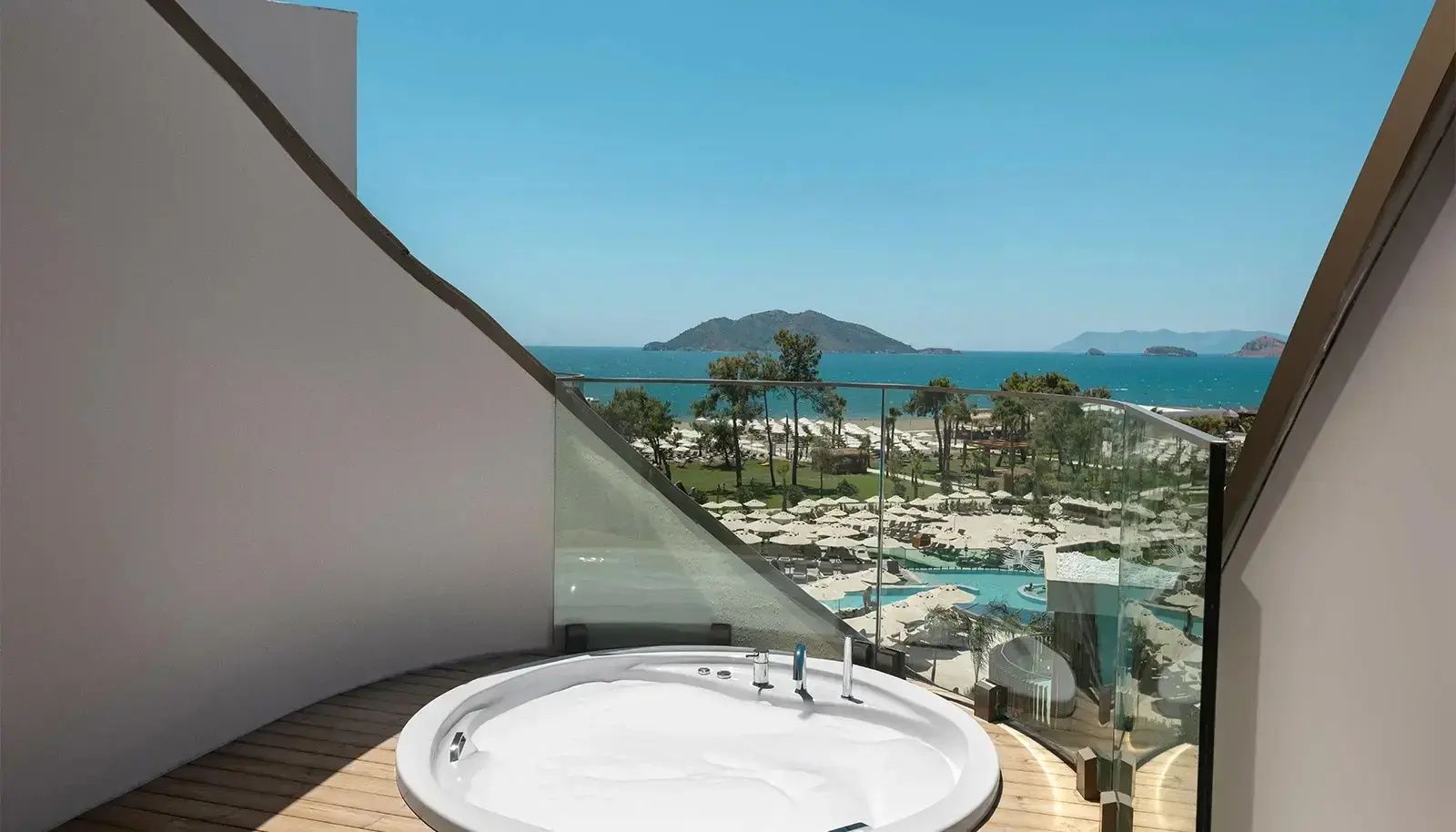 Runder Whirlpool auf einer Terrasse mit freiem Blick auf Garten, Pools und das Meer.