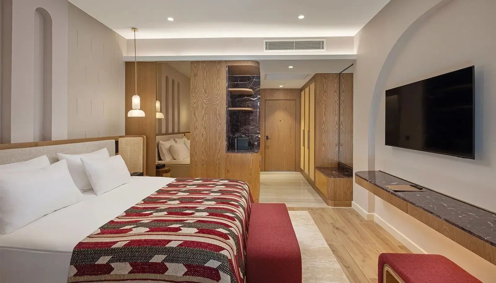 Hotelzimmer mit Doppelbett, roter Polsterbank und Einbauschränken aus Holz.