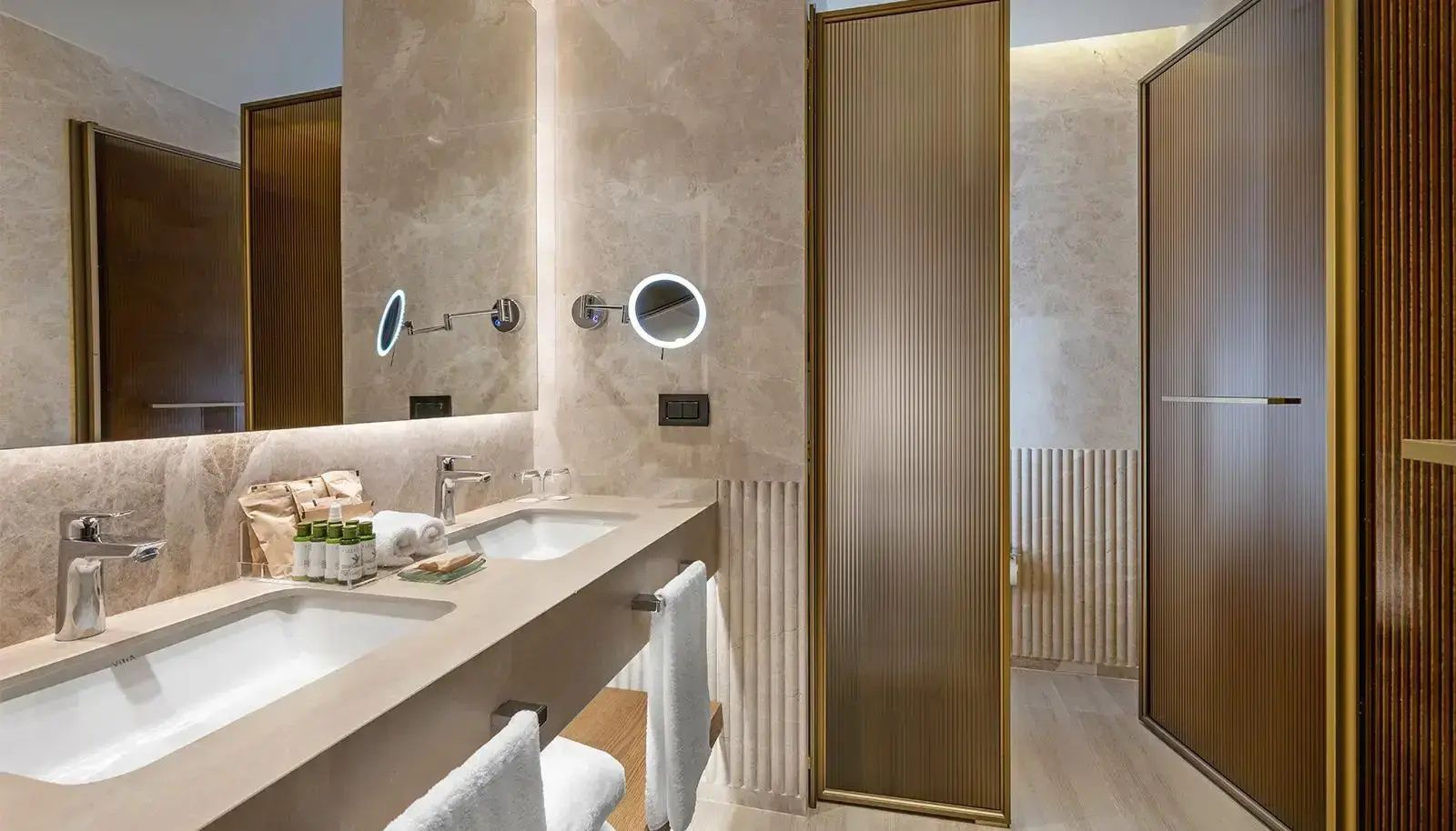 Badezimmer mit beigefarbenem Waschtisch, beleuchtetem Spiegel und Handtüchern.