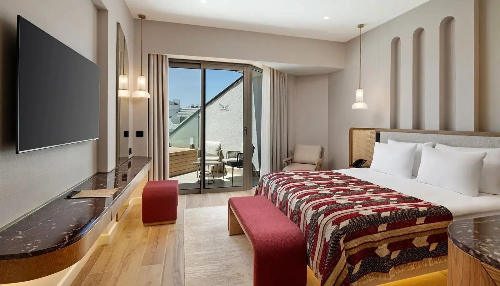 Zimmerinterieur mit Bett, Schminktisch und Zugang zum Balkon mit Sitzgelegenheiten.