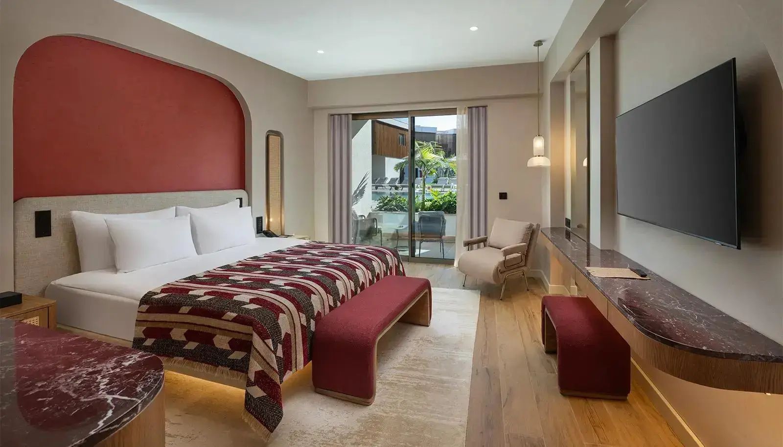 Modernes Hotelzimmer mit Doppelbett, Sesseln und Balkontür mit Blick auf die Außenanlage.