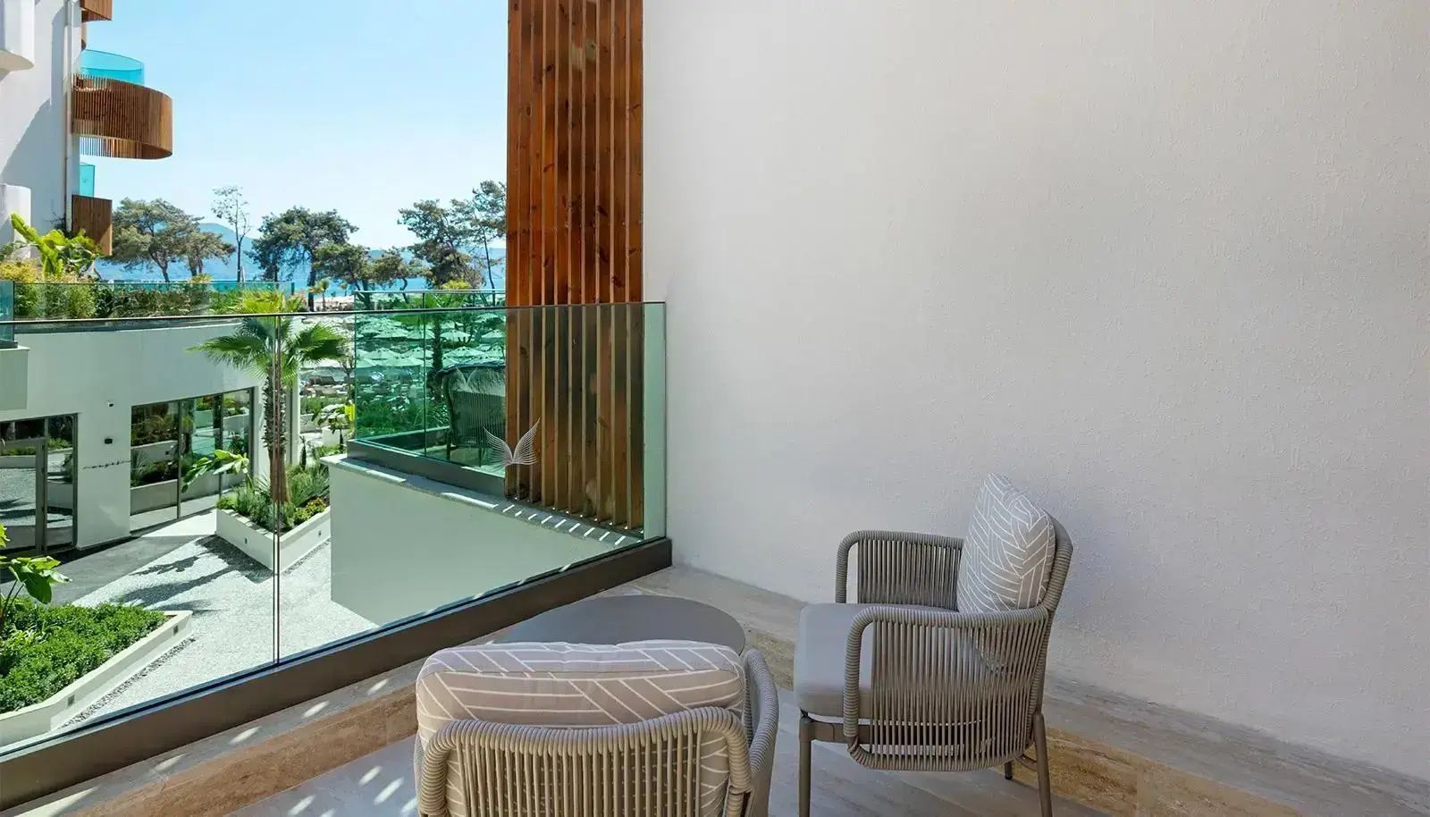 Balkon mit zwei grauen Sesseln, Glasgeländer und Ausblick auf Palmen.
