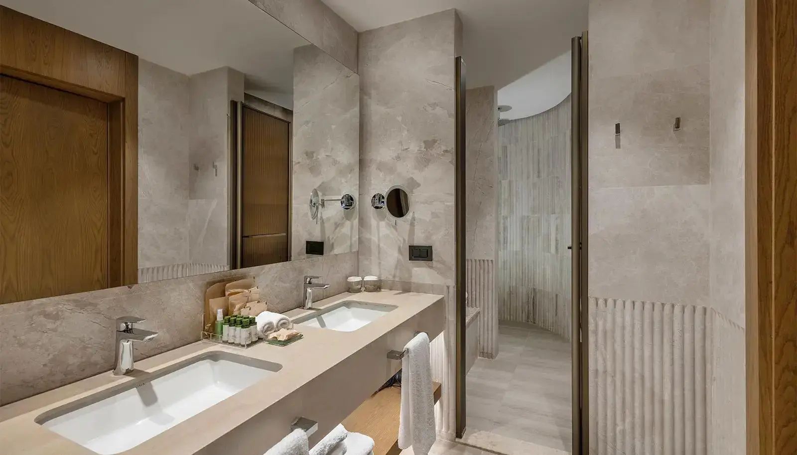 Moderner Waschtisch mit zwei Waschbecken, großem Spiegel und Blick in die angrenzende Dusche im Hotelbad.