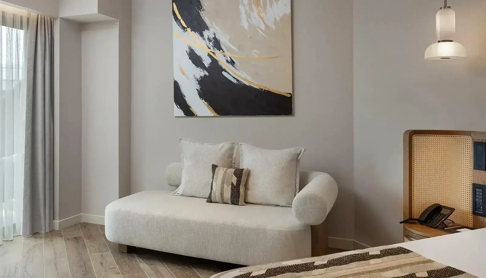 Helles Polstersofa mit Kissen unter einem abstrakten Wandbild in braun und gold.