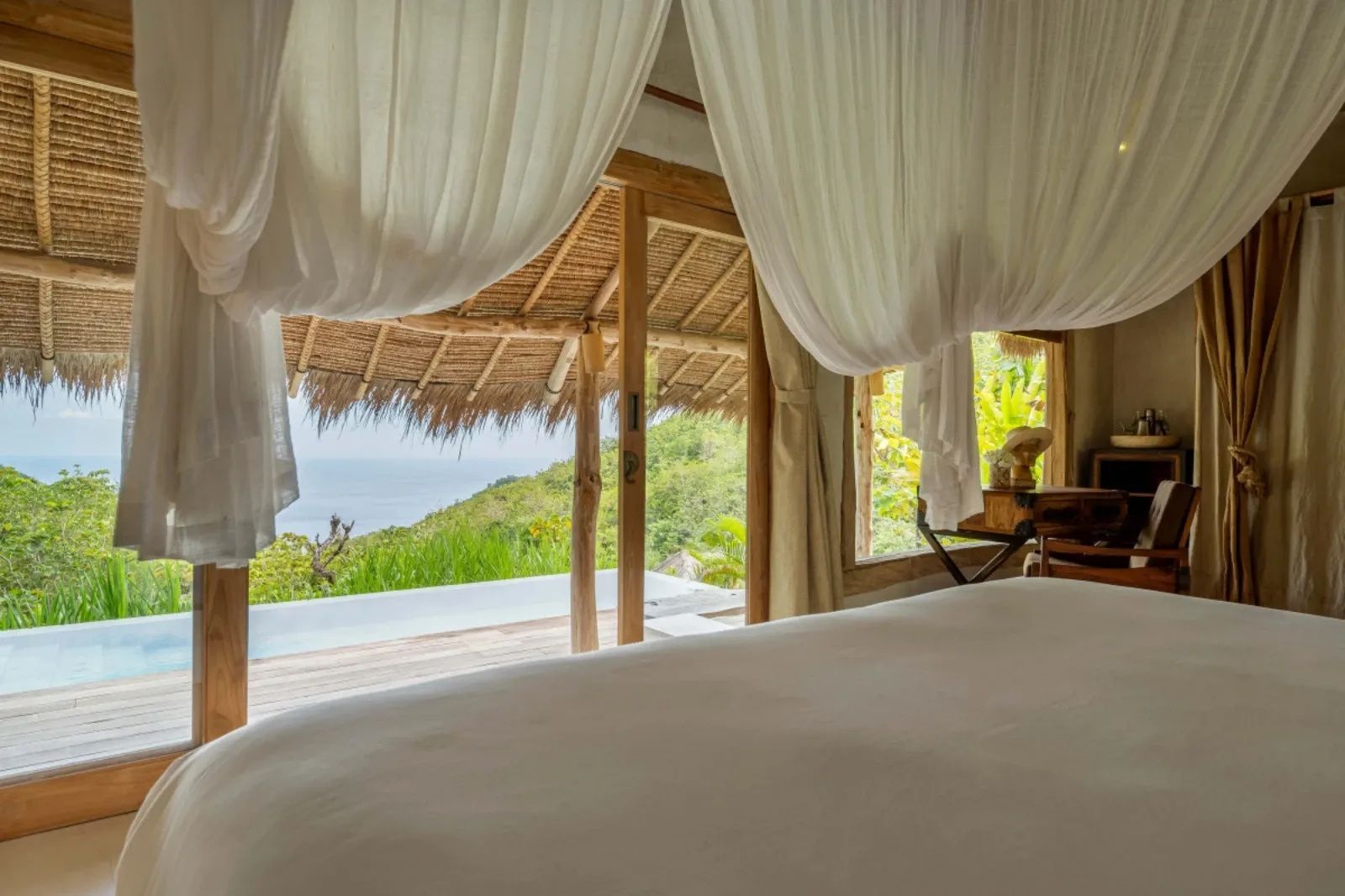 Blick vom Bett durch weißes Moskitonetz auf Terrasse mit Pool und Meer