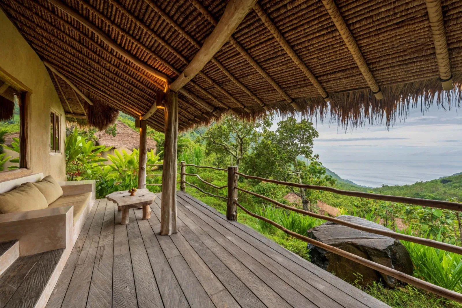 Überdachte Holzterrasse mit Reetdach und Blick auf grüne Hügel und das Meer.