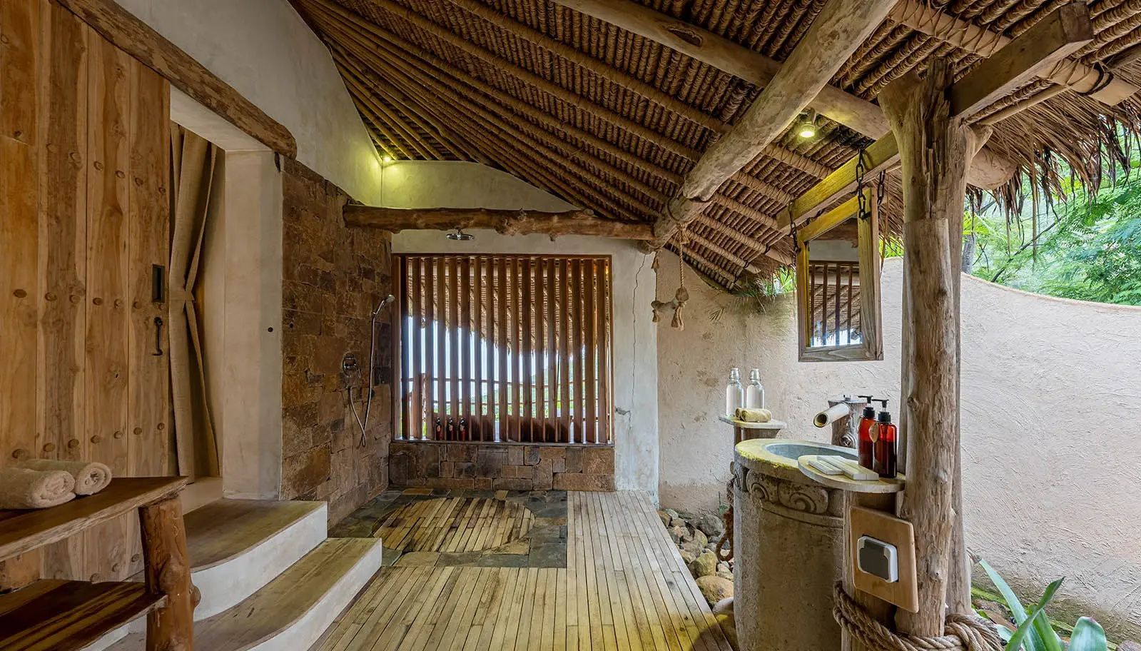 Halboffenes Badezimmer mit einer Regendusche, Holzlamellen, Waschtisch und Bambusdach.