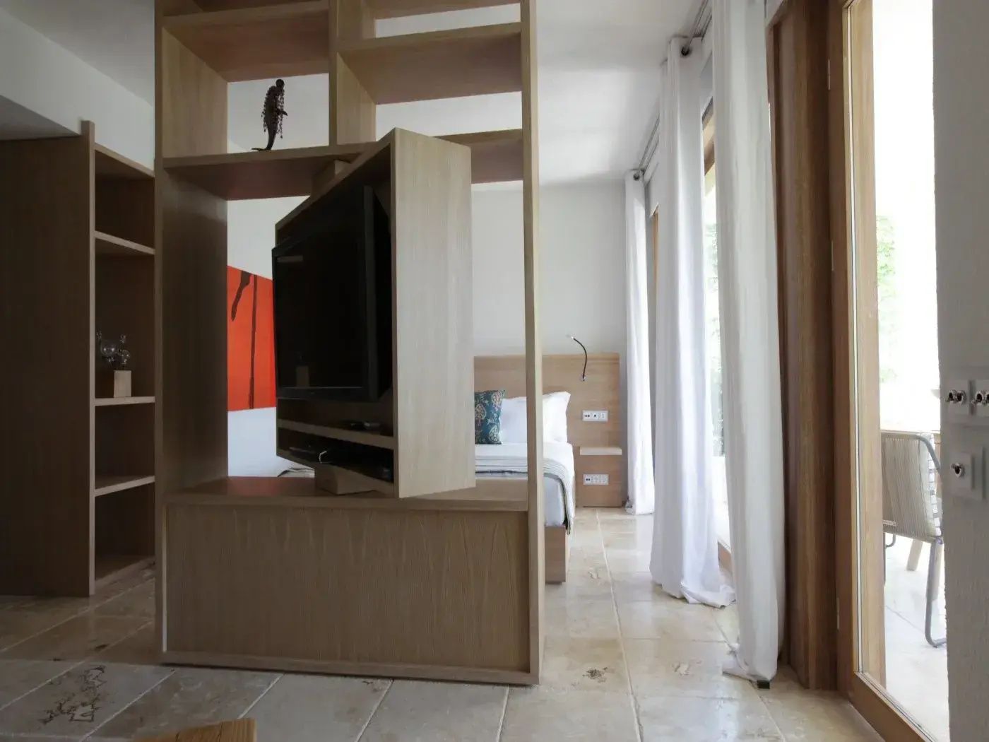 Raumteiler aus hellem Holz mit drehbarem Fernseher zwischen Wohn- und Schlafbereich.