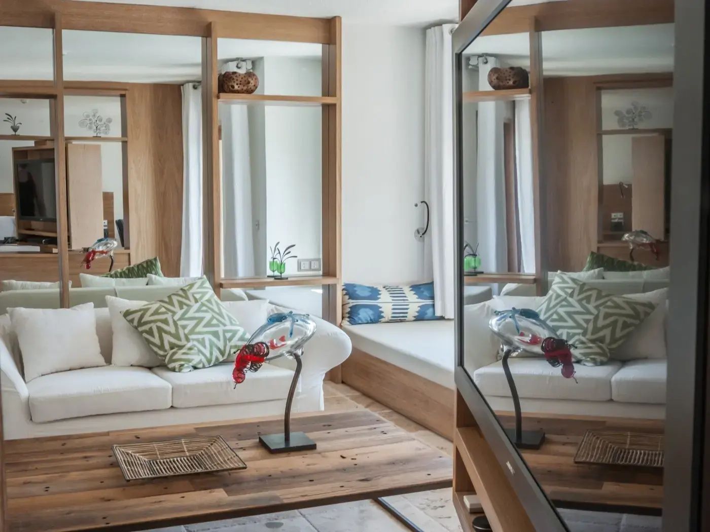 Wohnbereich mit weißem Sofa, gemusterten Kissen, Holztisch und einer Sitzbank.