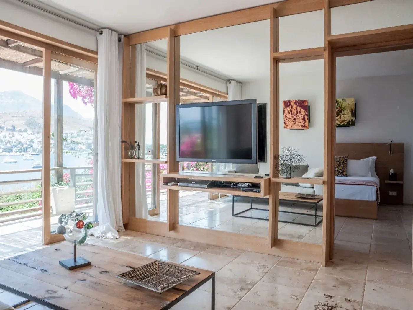 Wohnzimmerbereich mit TV an einer Holzwand und Blick durch Glasschiebetüren.