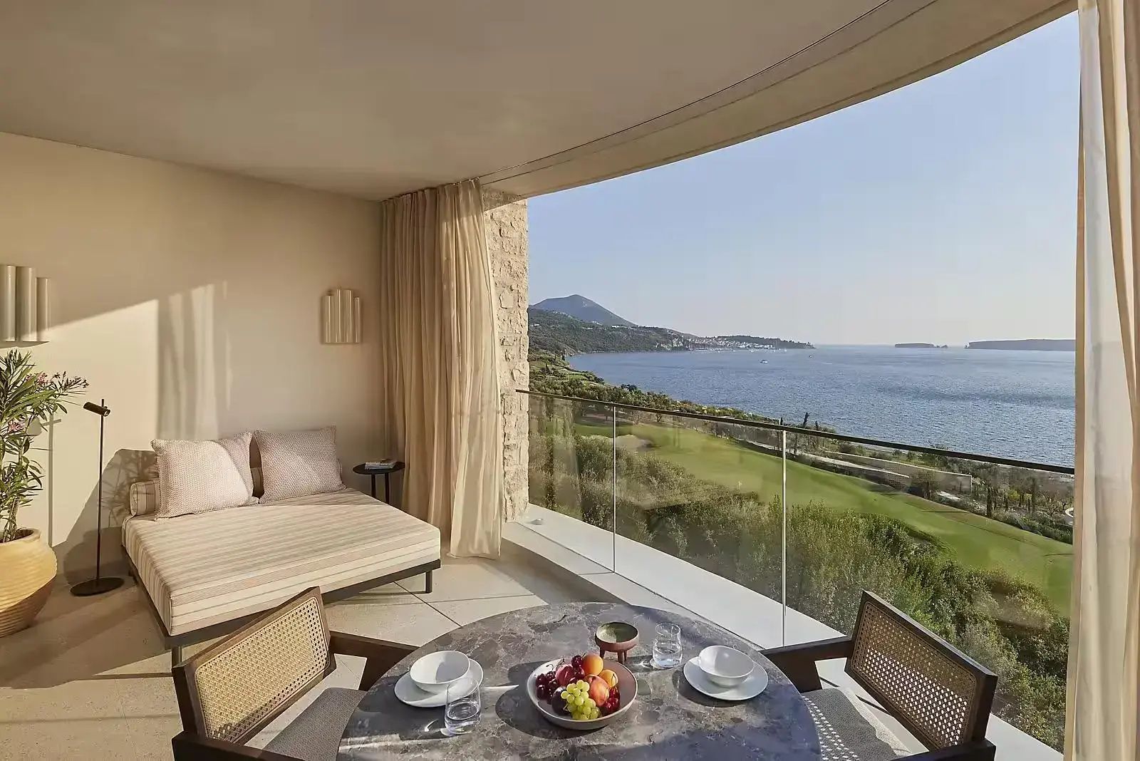 Überdachter Balkon mit Esstisch und Liege sowie Panoramablick auf die Küste und das Meer.