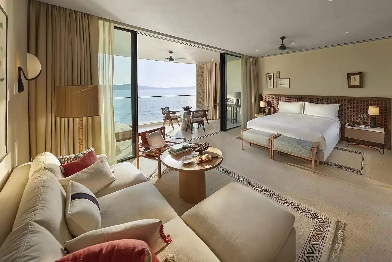 Hell eingerichtetes Hotelzimmer mit Doppelbett, Sofaecke und großem Balkon mit Meerblick.