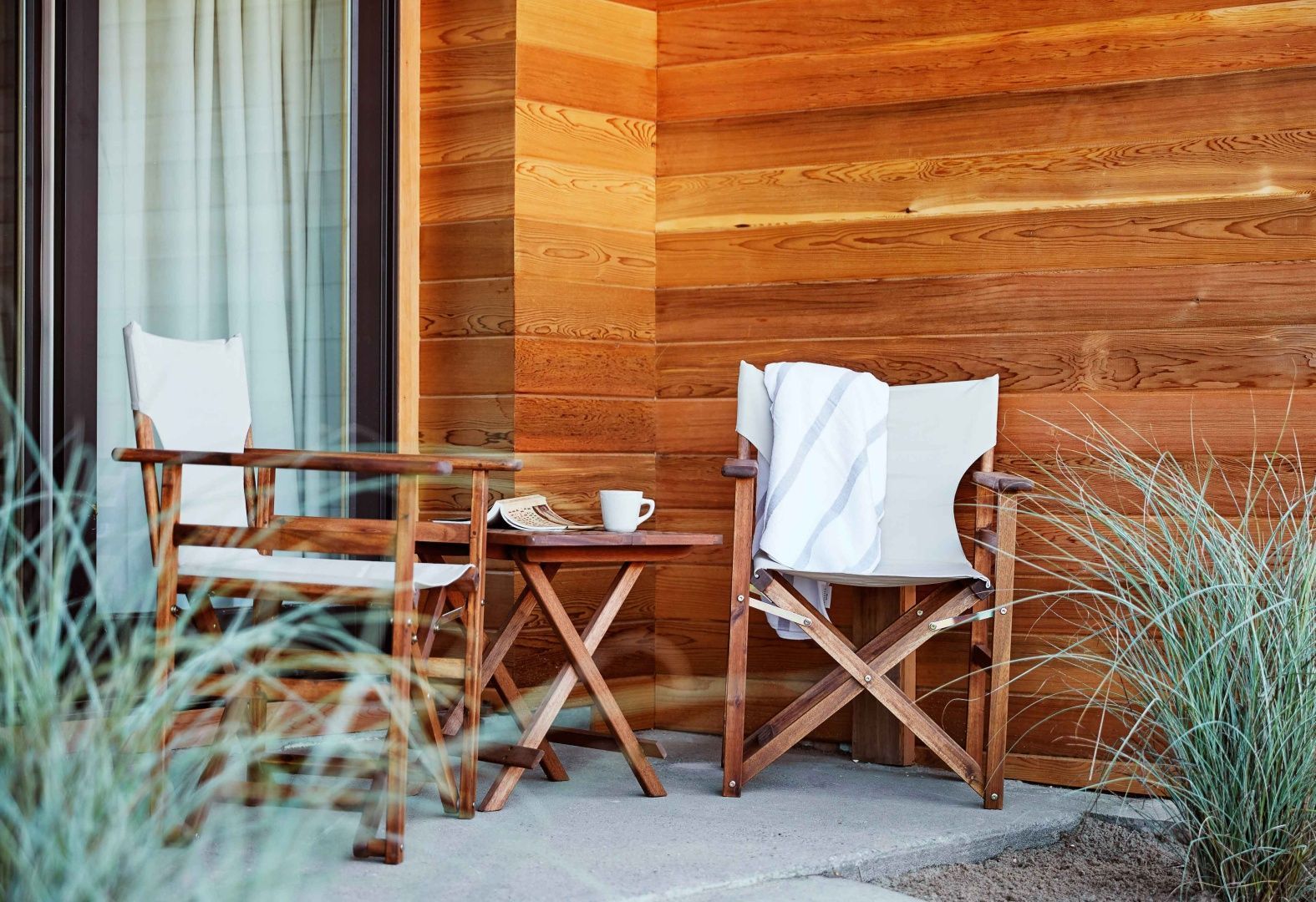 Holzsessel und ein kleiner Tisch auf einer Terrasse vor einer Holzfassade.