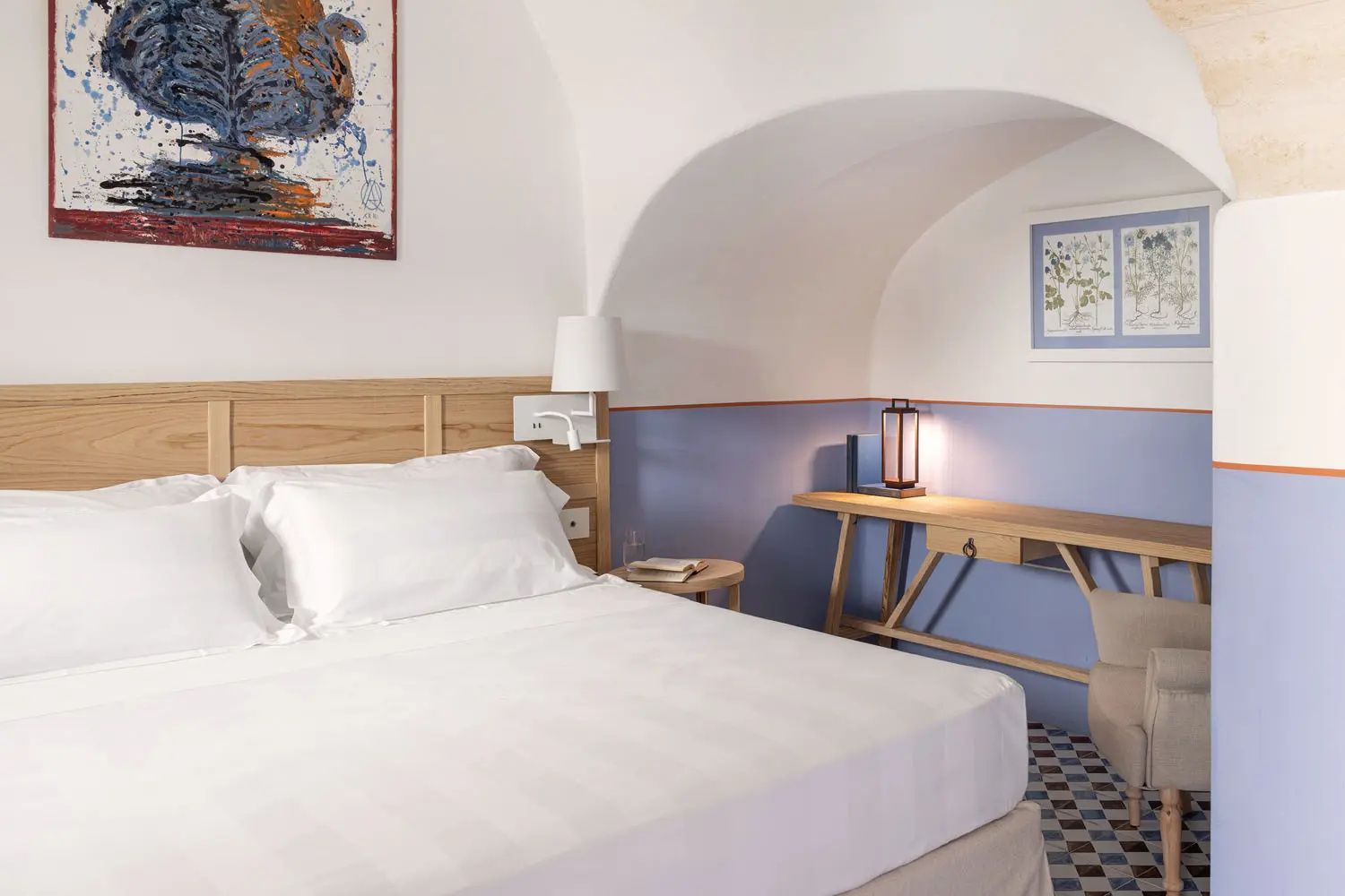 Doppelbett und ein Holzschreibtisch an einer blau gestrichenen Wand unter einem Rundbogen.