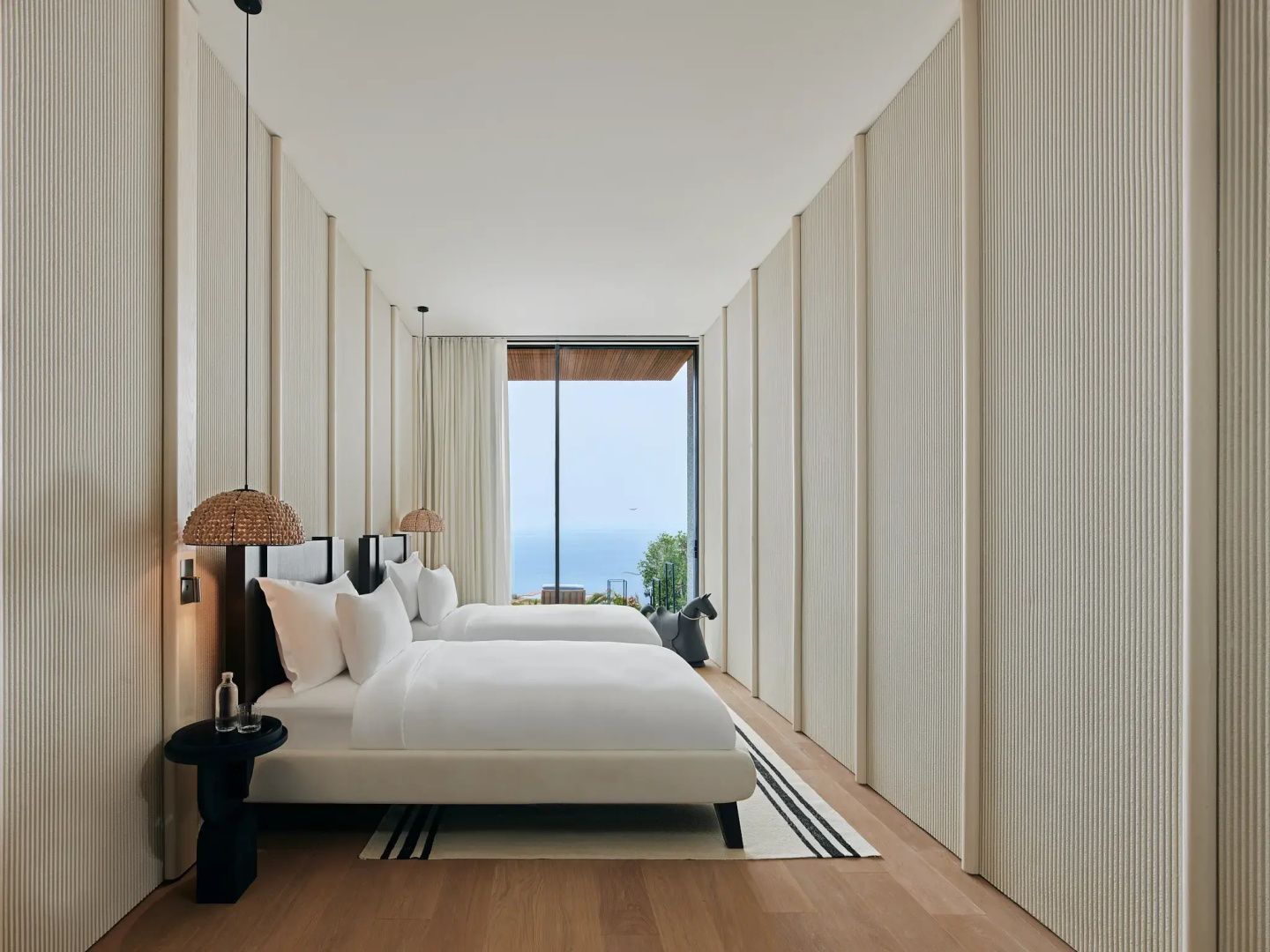 Helles Schlafzimmer mit zwei Einzelbetten, Holzfußboden und Ausblick auf das Meer.