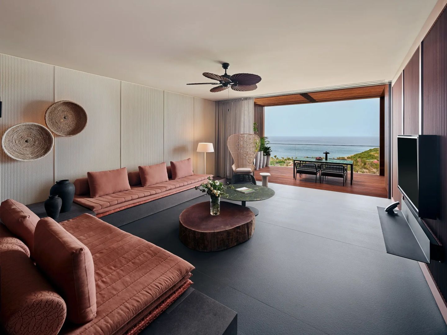 Modernes Wohnzimmer mit terracottafarbenen Polstern und Terrasse mit Meerblick.