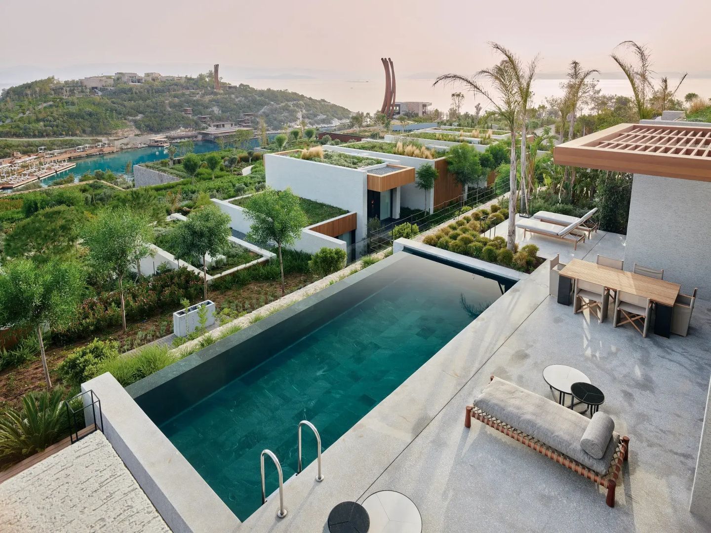 Terrasse mit privatem Swimmingpool, Liegestühlen, begrünten Dächern und Blick aufs Meer.