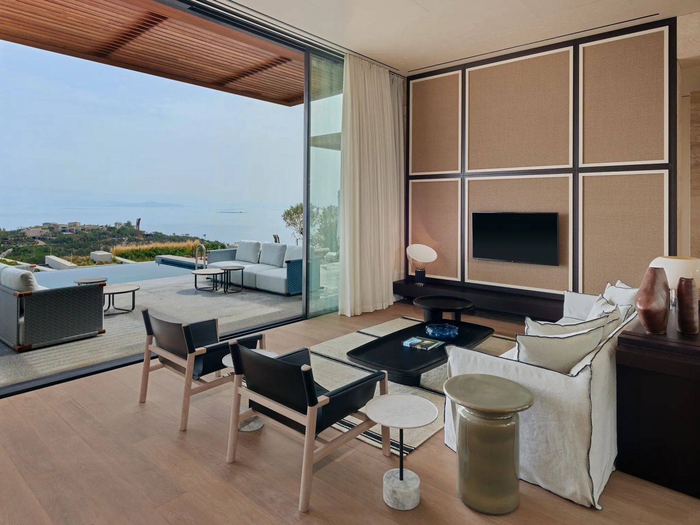 Wohnbereich einer Suite mit TV-Wand, Sitzmöbeln und großer Glasfront zur Terrasse.