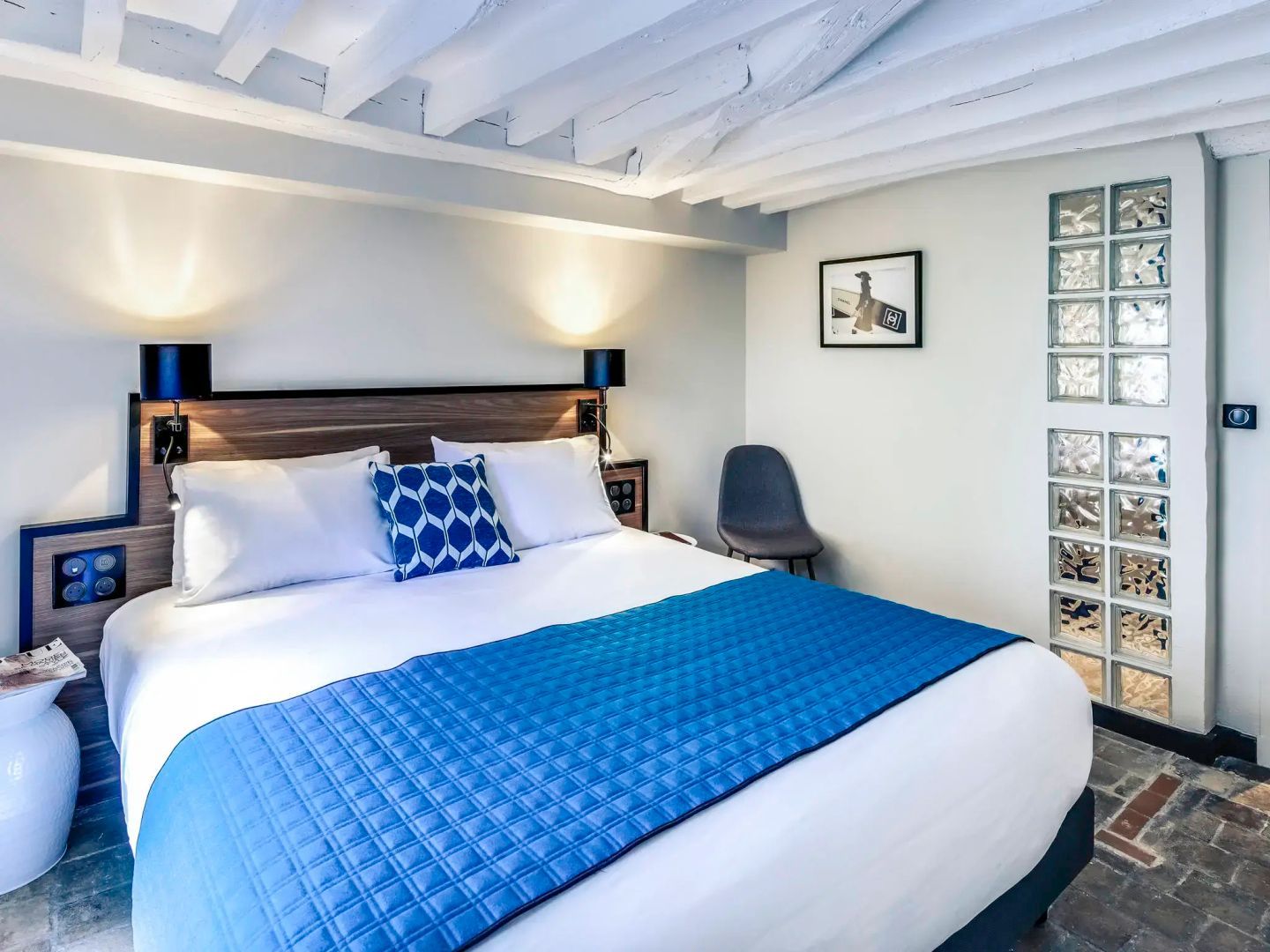 Doppelbett mit blauer Tagesdecke in einem hellen Zimmer mit Holzbalkendecke