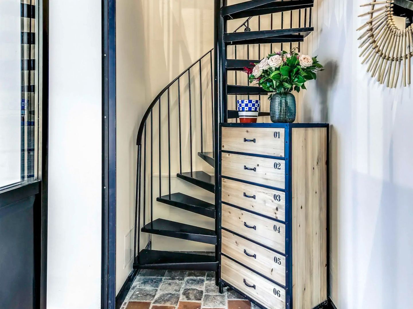 Schwarze Wendeltreppe neben einer Holzkommode mit durchnummerierten Schubladen.