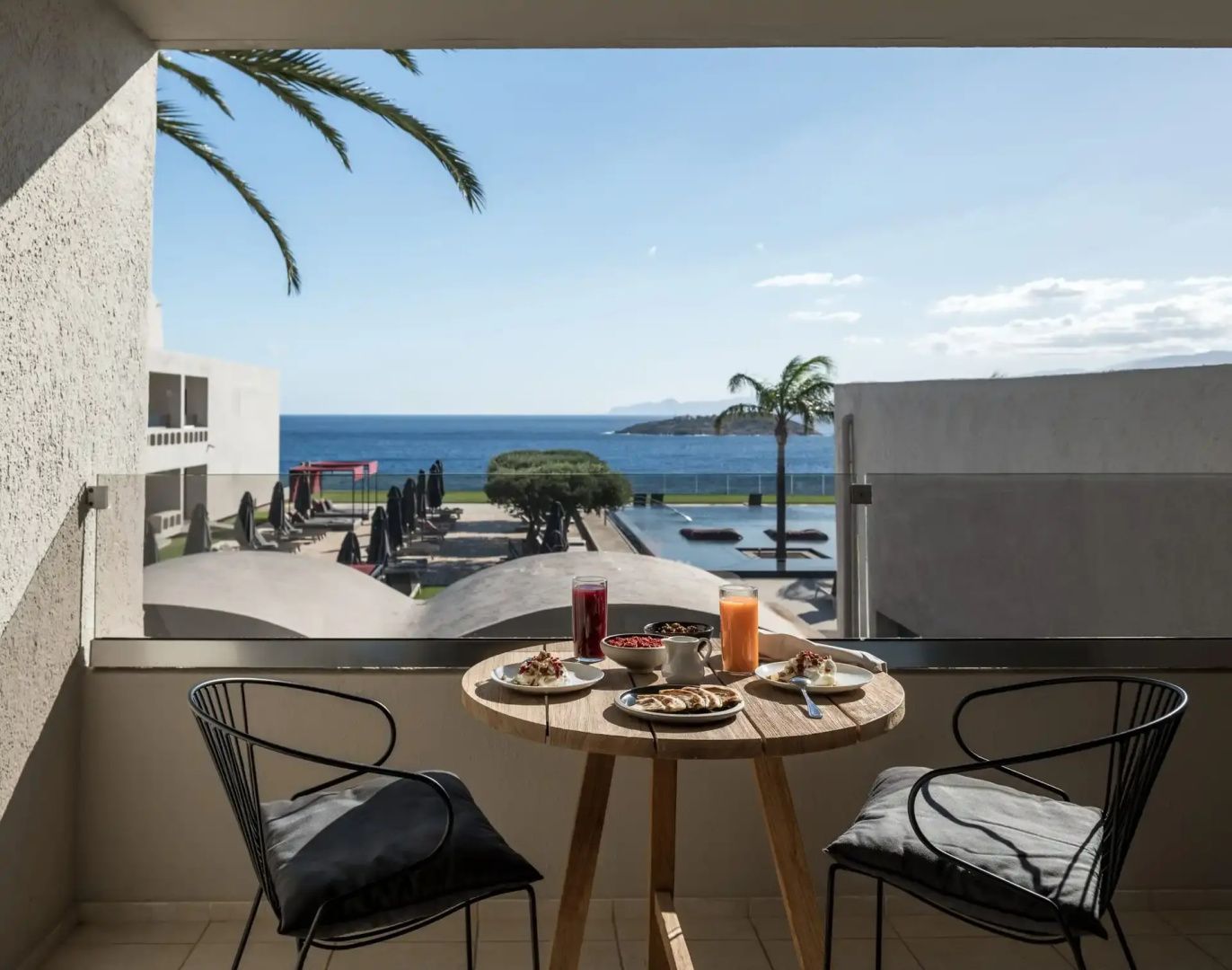 Gedeckter Tisch auf dem Balkon mit Ausblick auf die Poolanlage der Anlage und das Meer.