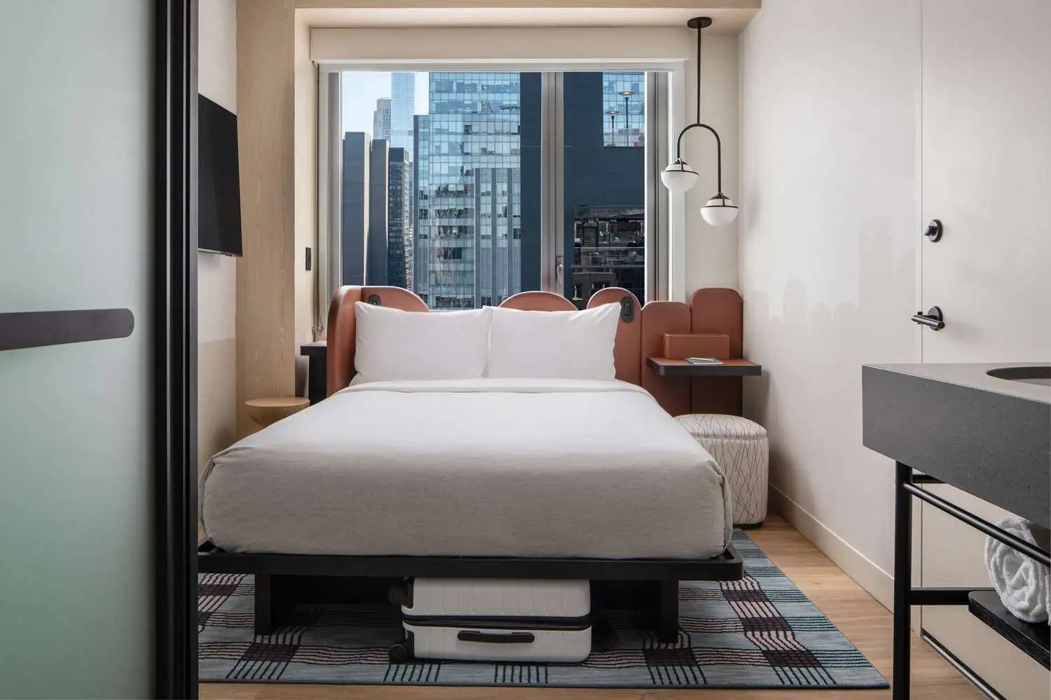 Modernes Hotelzimmer mit Doppelbett, Fensterfront und Blick auf die Hochhäuser von New York City.