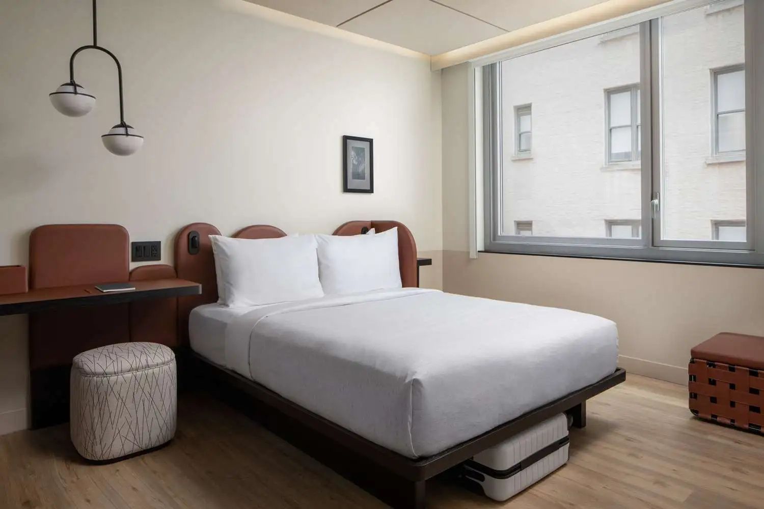 Hell eingerichtetes Hotelzimmer mit Doppelbett, Nachttisch und einem großen Fenster.