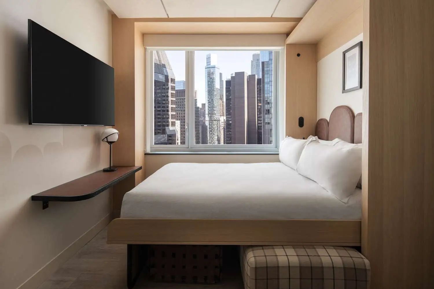 Gemütliches Hotelzimmer mit Doppelbett, Wandfernseher und Blick auf Hochhäuser durch das Fenster.