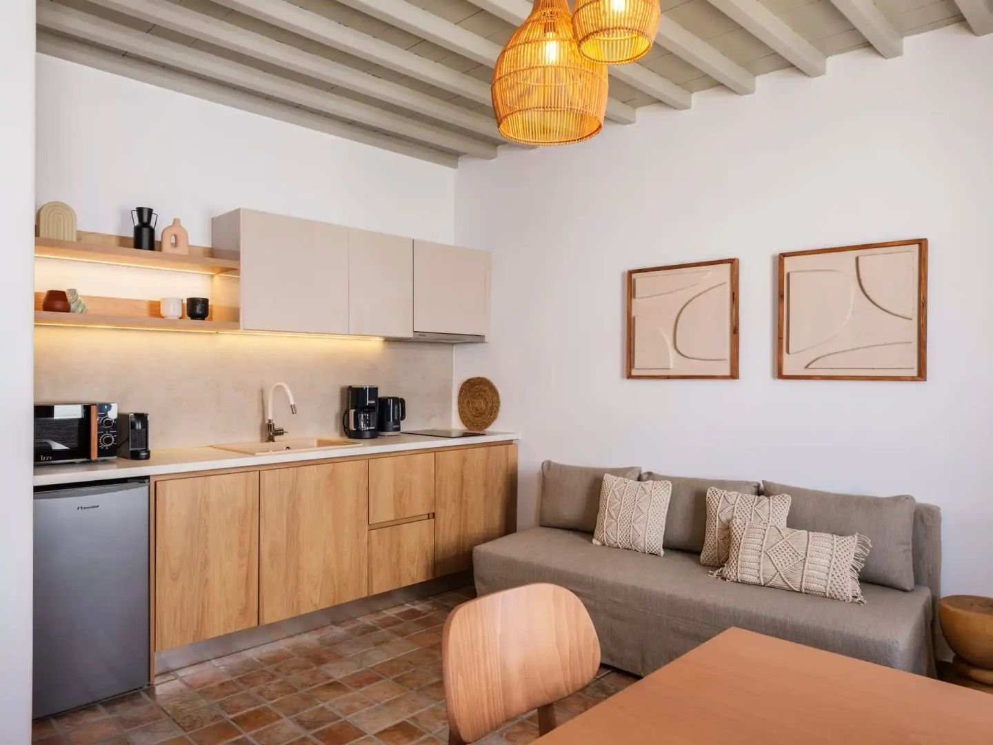Küchenzeile aus Holz mit Kaffeemaschine neben einem beigefarbenen Sofa und Esstisch.