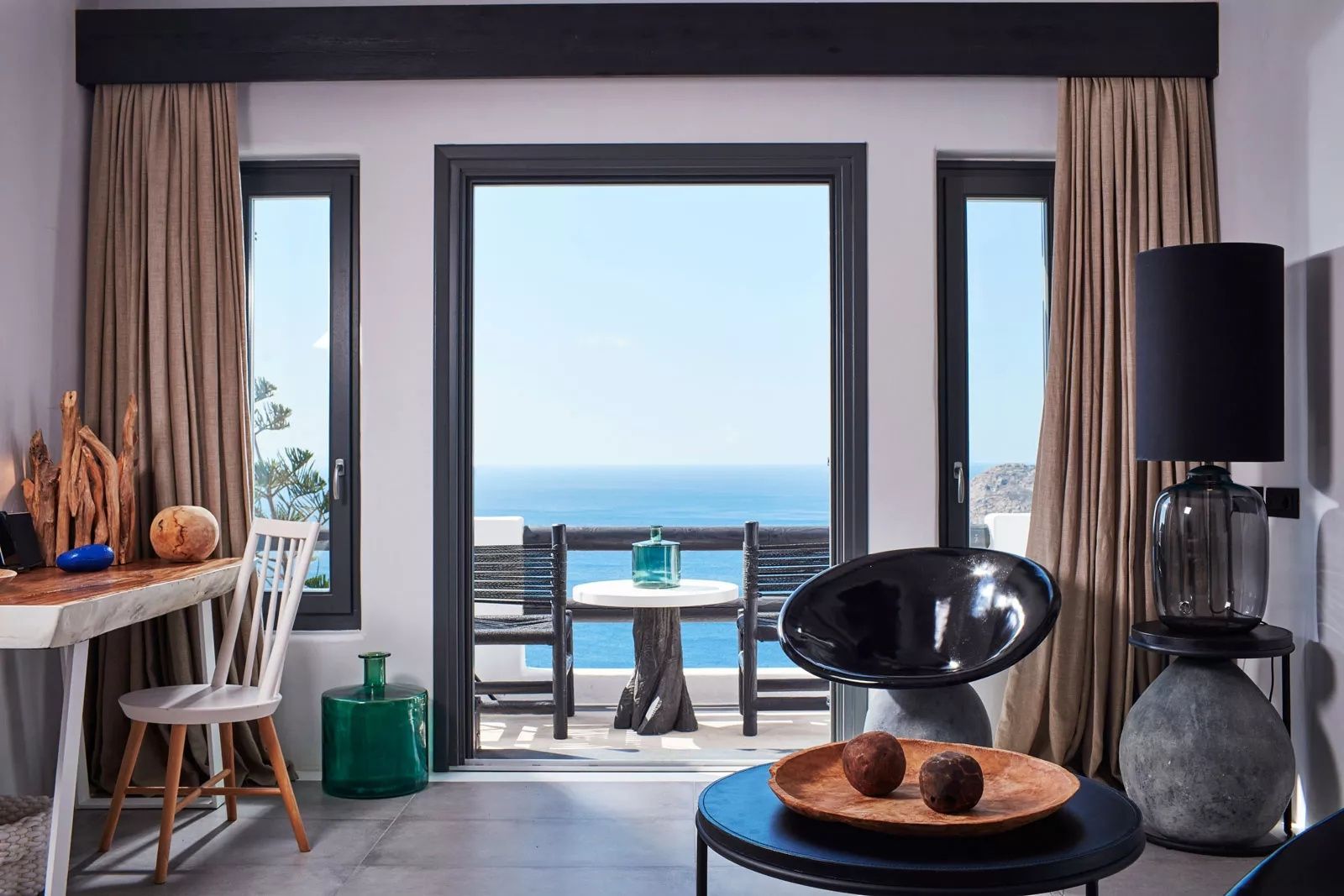 Blick durch die geöffnete Terrassentür auf das blaue Meer und einen Tisch auf dem Balkon.