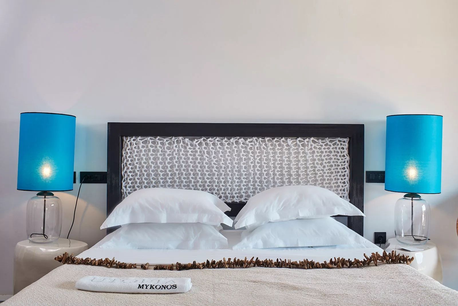 Doppelbett mit weißen Kissen, dunklem Kopfteil und dekorativem Band.