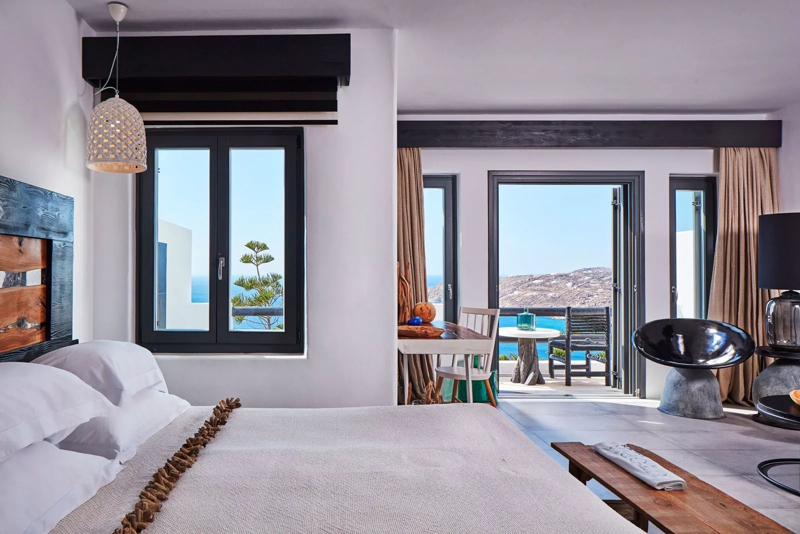 Schlafzimmer mit Doppelbett, Schreibtisch und geöffneter Balkontür mit Blick auf das Meer.