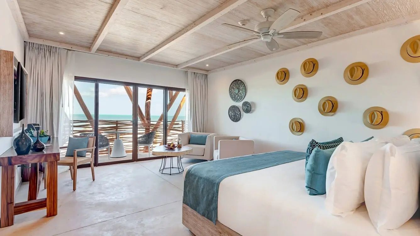 Helles Hotelzimmer mit Doppelbett, Sitzbereich und Balkontür mit Meerblick.