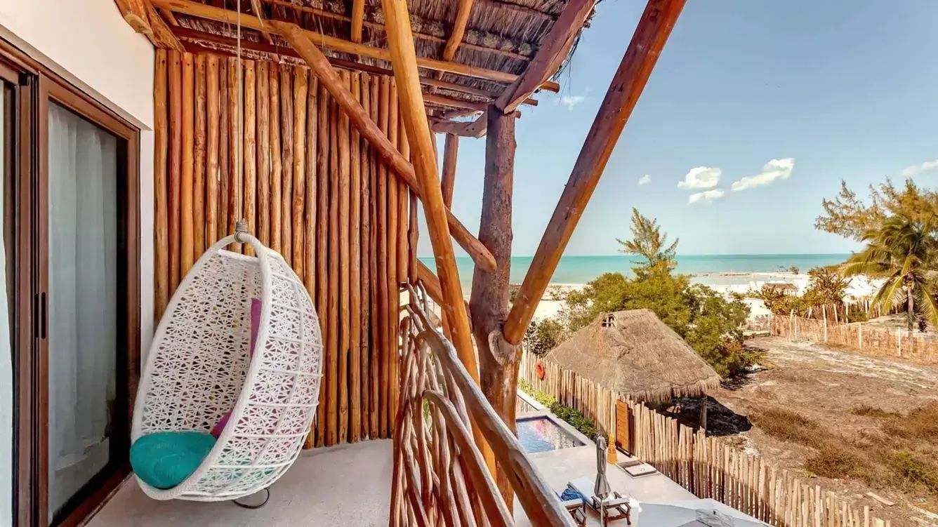 Balkon mit weißem Hängesessel und einem Holzgeländer mit Blick auf Strand und Meer.