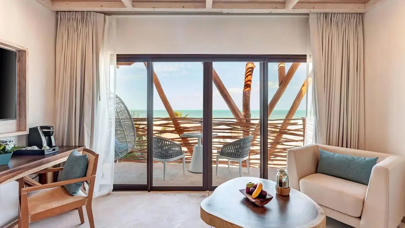 Blick durch große Glasschiebetüren auf eine Terrasse mit Sitzmöbeln und Meer.