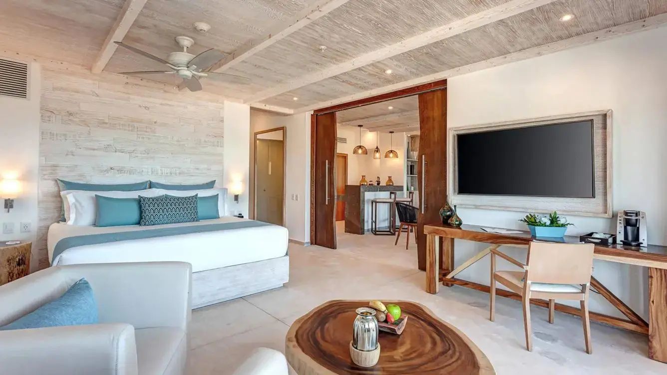 Großzügiger Wohnbereich der Suite mit Holzcouchtisch, Fernseher und Schiebetür.