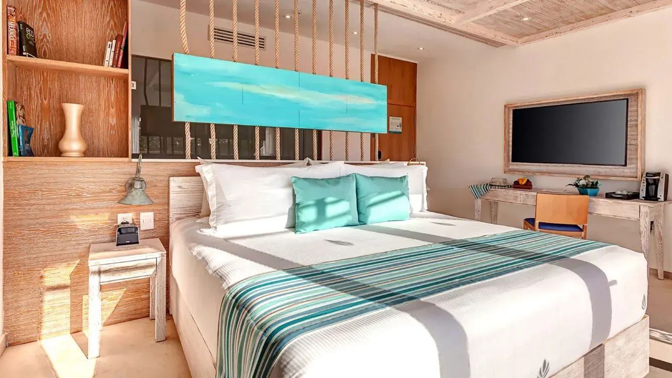 Helles Hotelzimmer mit großem Doppelbett, türkisfarbenen Akzenten und Holzdekor.