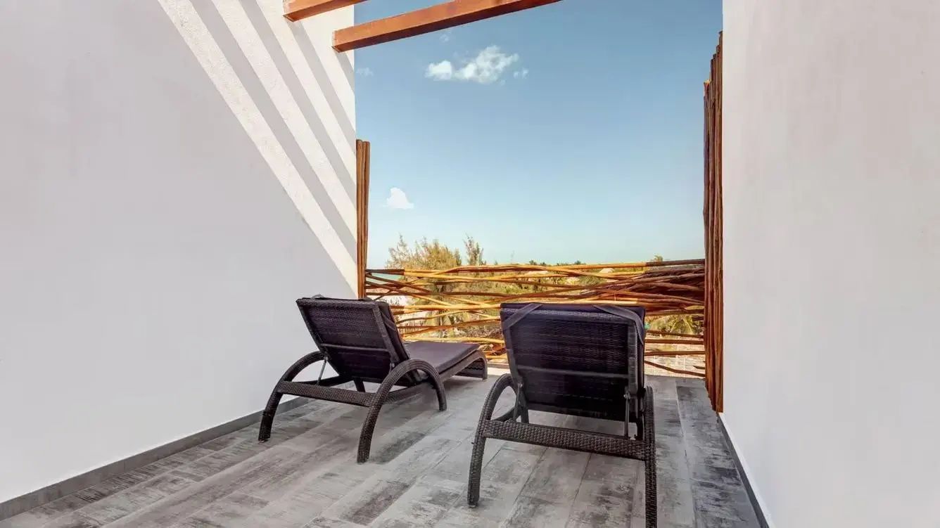 Dachterrasse mit zwei dunklen Sonnenliegen und Holzgeländer unter blauem Himmel.