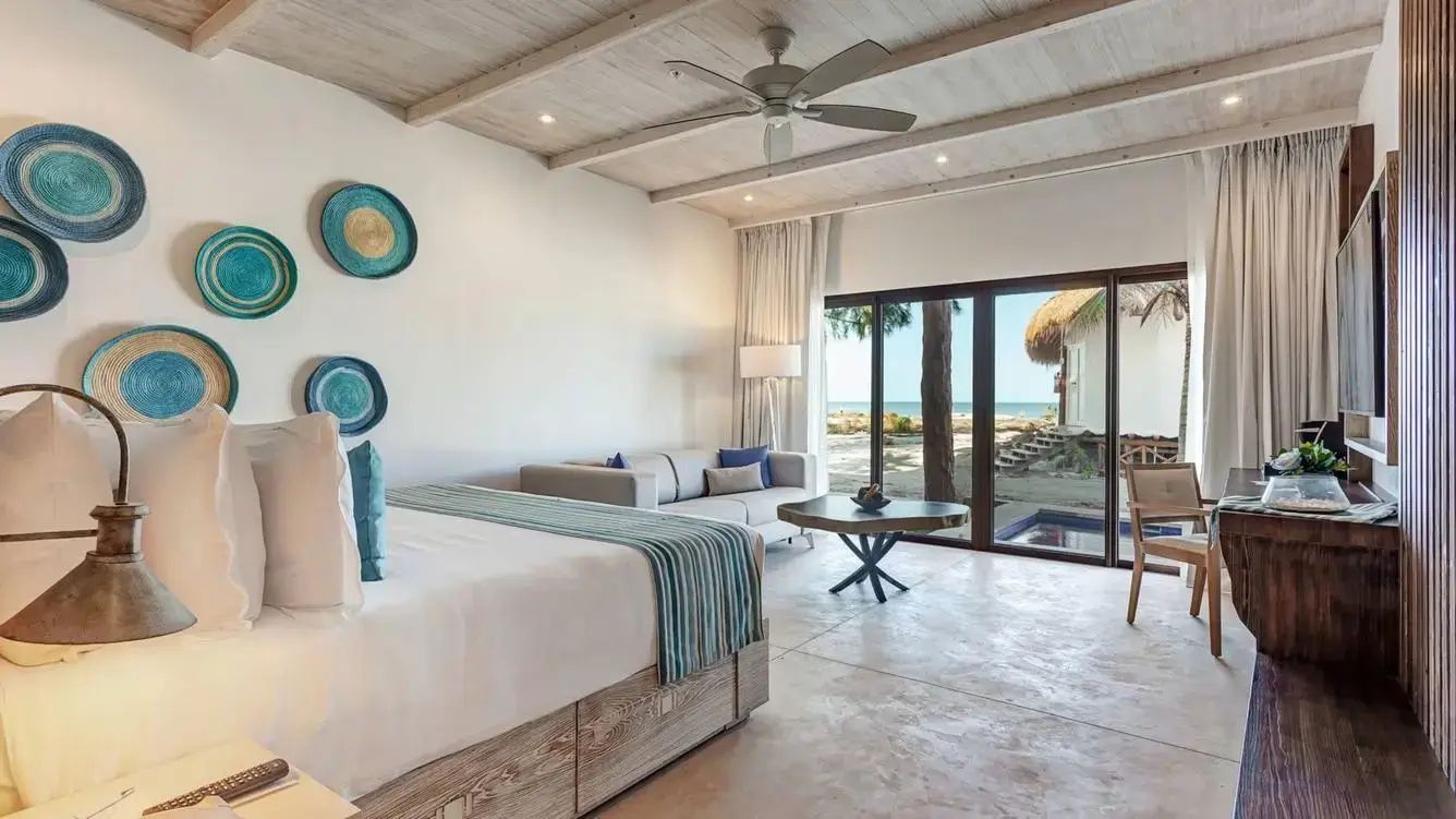 Blick aus dem Zimmer durch große Schiebetüren auf den Sandstrand und das Meer.