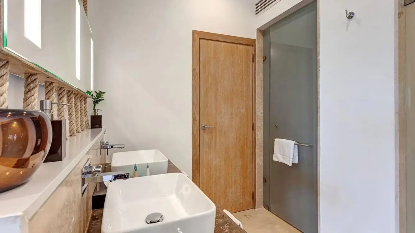 Badezimmer mit zwei weißen Aufsatzwaschbecken, Spiegel und einer Holztür.
