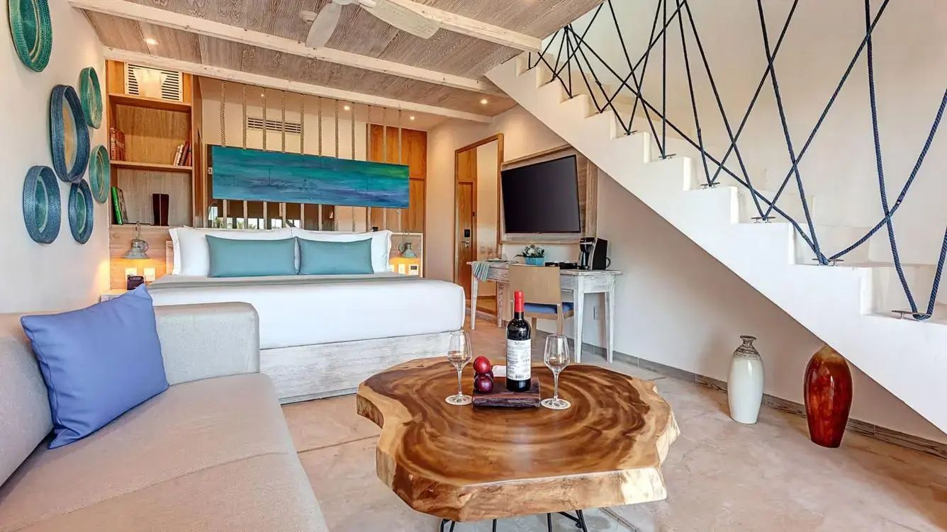 Wohnbereich der Suite mit Holztisch, Wein und Treppe zum oberen Stockwerk.
