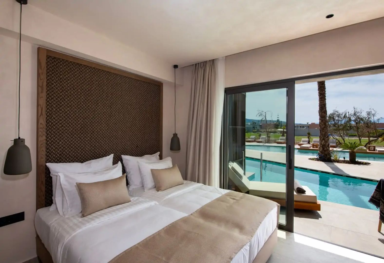 Helles Hotelzimmer mit Doppelbett und direktem Zugang zum Swimmingpool durch eine Glas-Schiebetür.