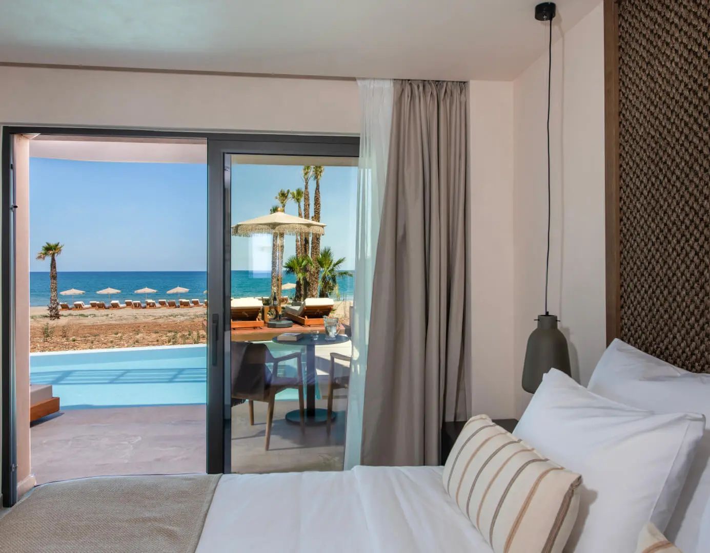 Blick aus dem Zimmer über die Terrasse und den Pool hinweg auf den Strand und das Meer.