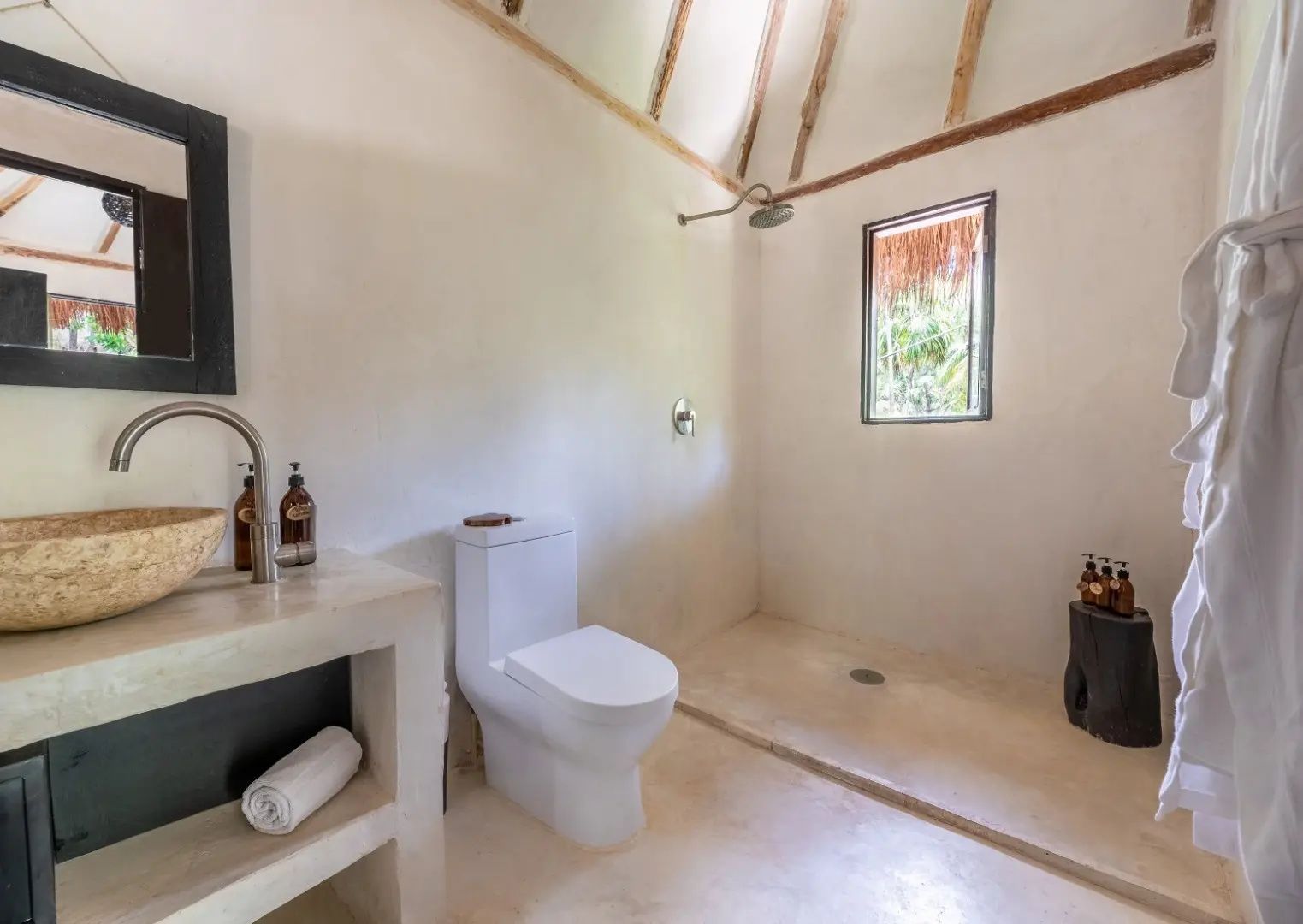Badezimmer mit bodengleicher Dusche, weißer Toilette und Waschtisch aus Stein.